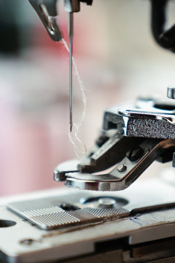 about-me Detailed view of a sewing machine needle with thread, poised for stitching.