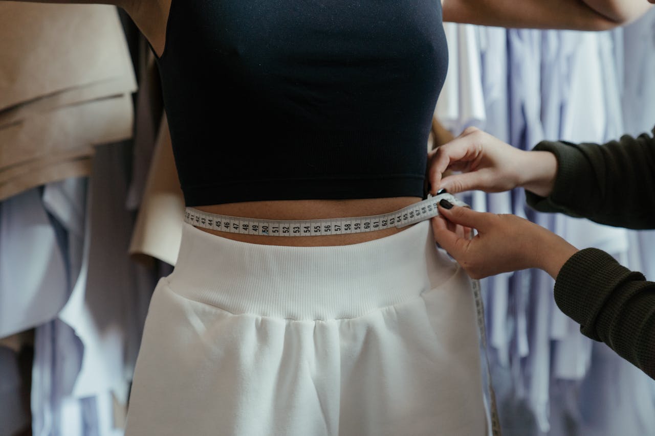 service-01 Detailed view of a tailor measuring a client's waist in a clothing workshop, focusing on precision.