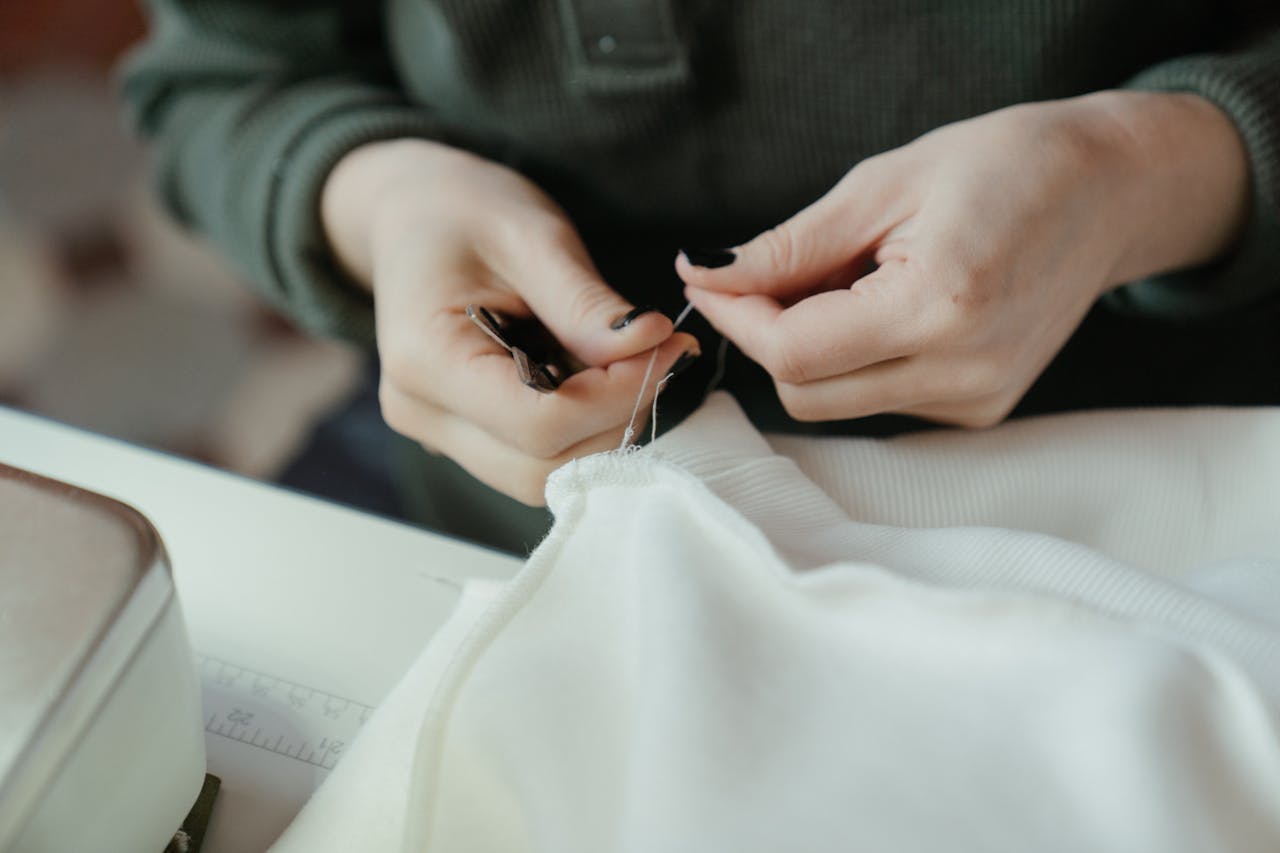 service-02 Close-up of hands sewing fabric with a needle and thread, showcasing careful craftsmanship.